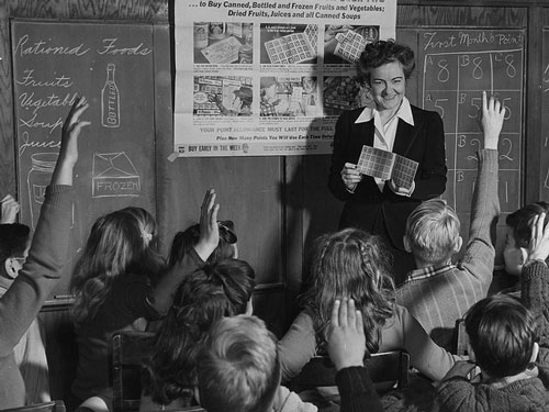 A classroom setting with a teacher and students. The image is in black and white  